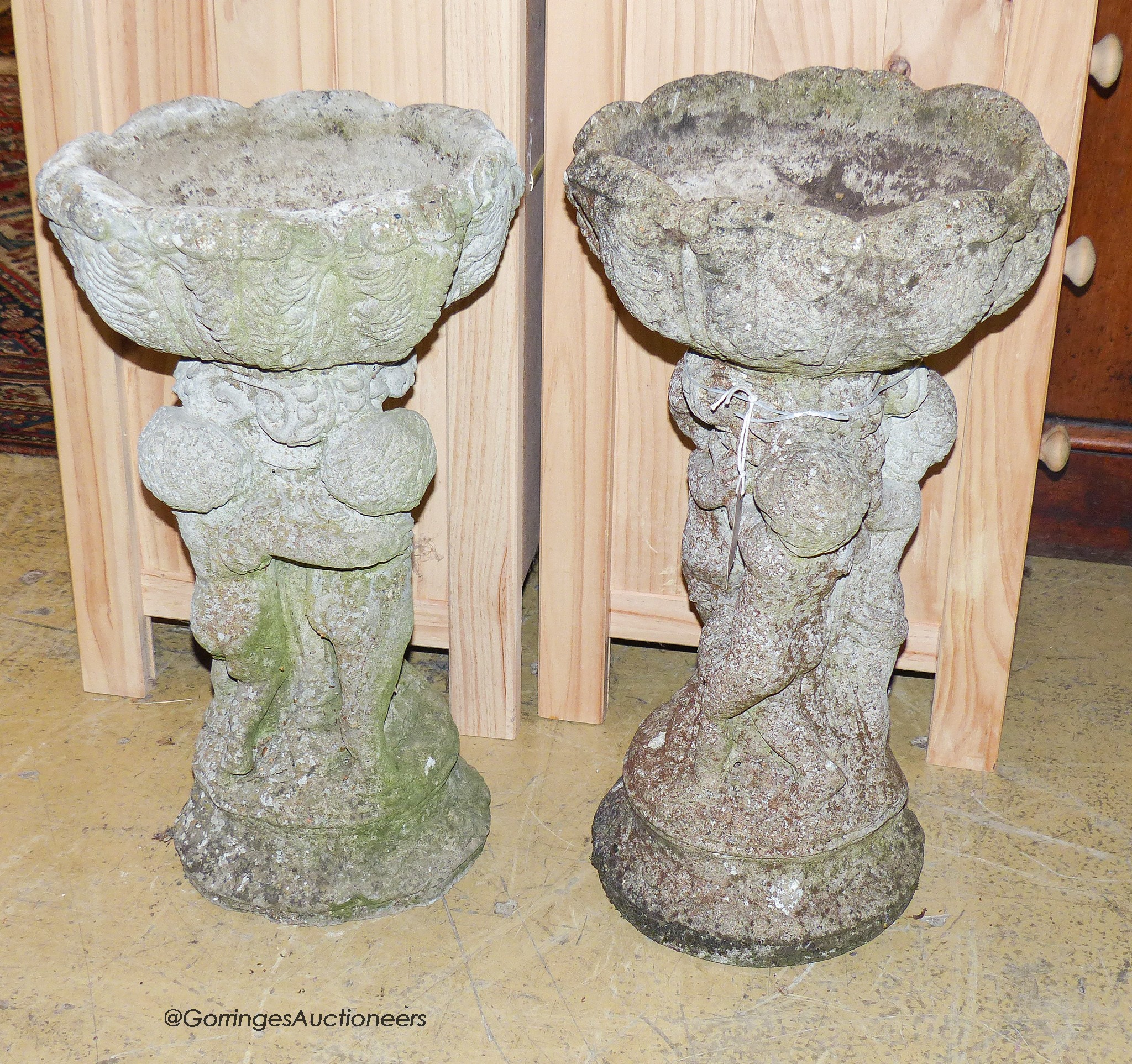A pair of reconstituted stone circular tulip form planters on figural cherub plinths, diameter 29cm, height 55cm